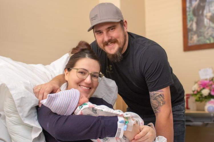 a dad and mom smiling at the camera holding their newborn baby